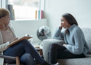 Two women sitting on a couch talking to each other.