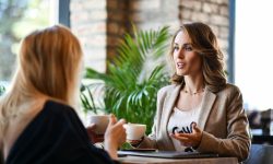 Two women are sitting at a table having coffee.